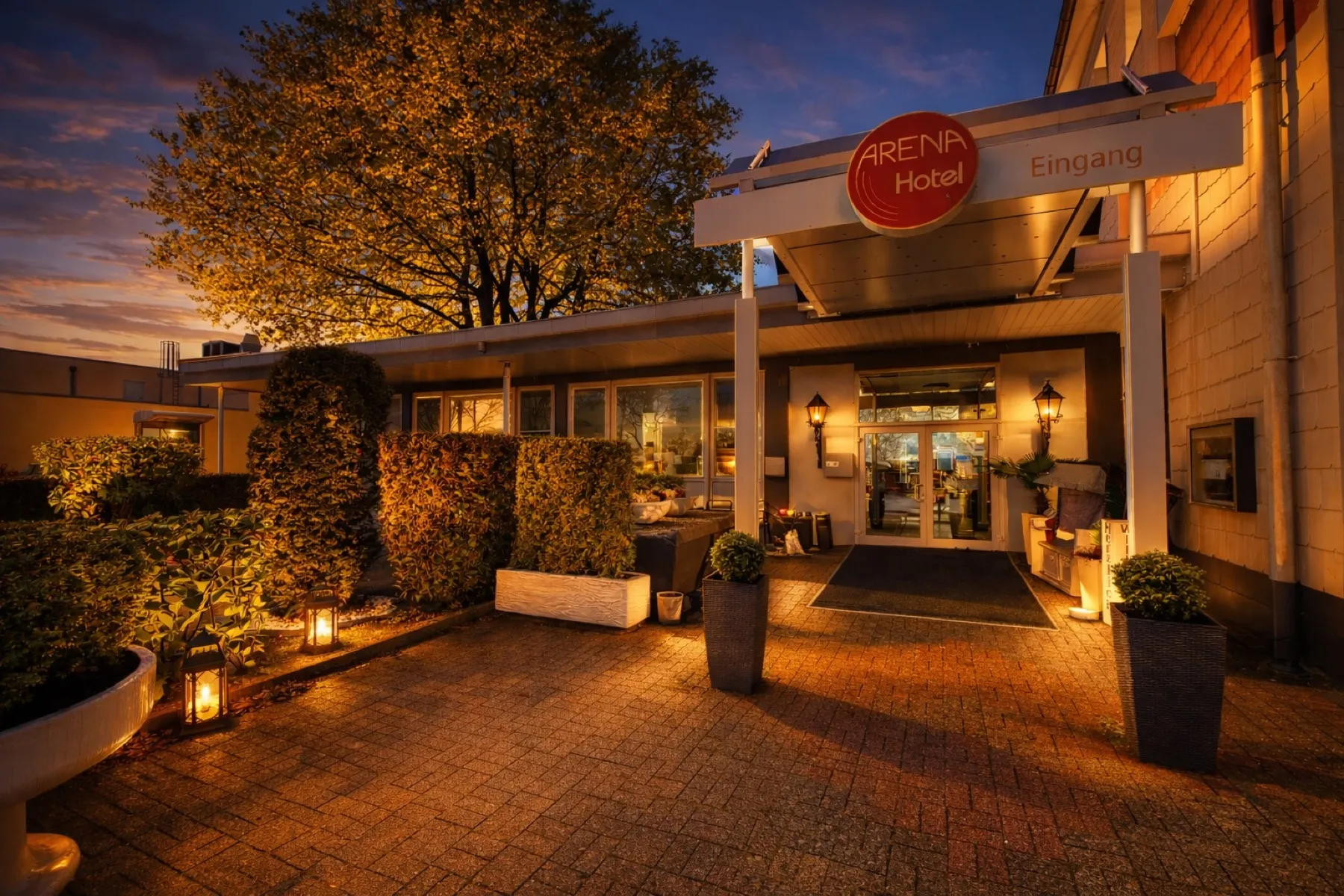 Eingang des Arena Hotels am Abend mit beleuchtetem Schild